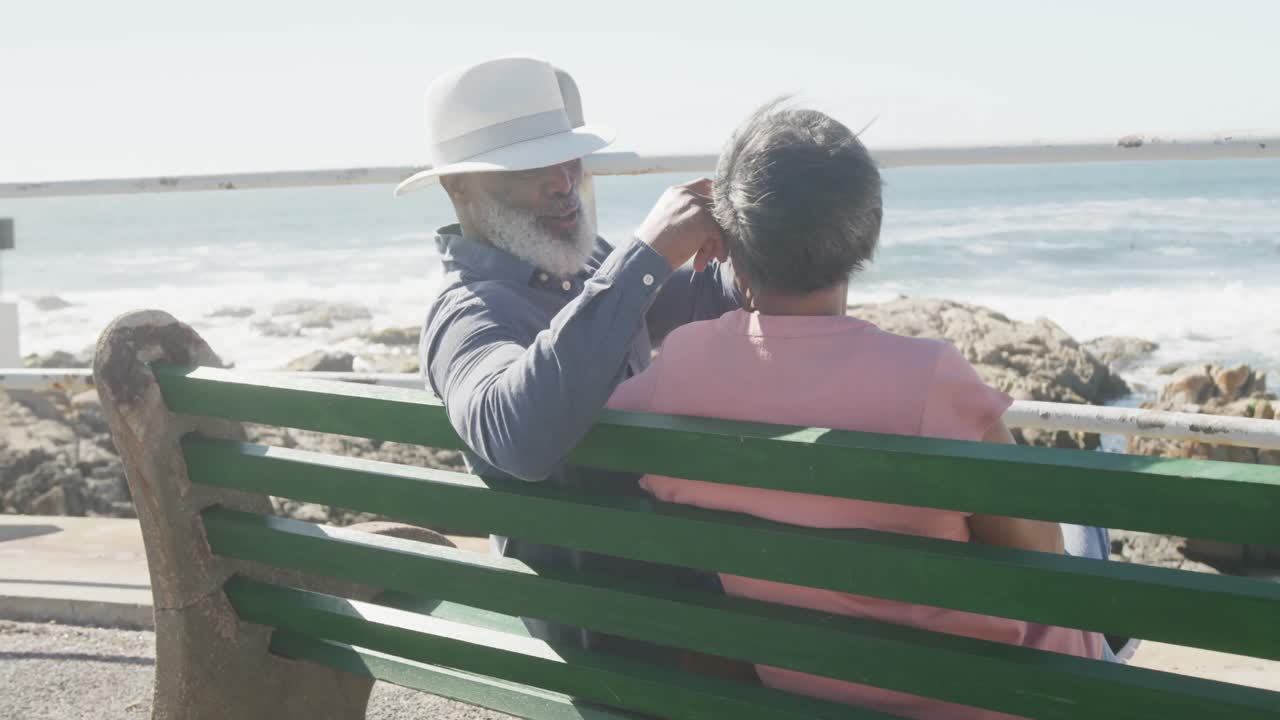 feliz pareja de ancianos afroamericanos sentados en un banco en el paseo marítimo, cámara lenta