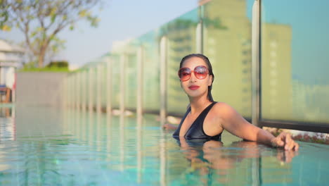 young asian woman with vintage sunglasses relaxing in roof pool of hotel