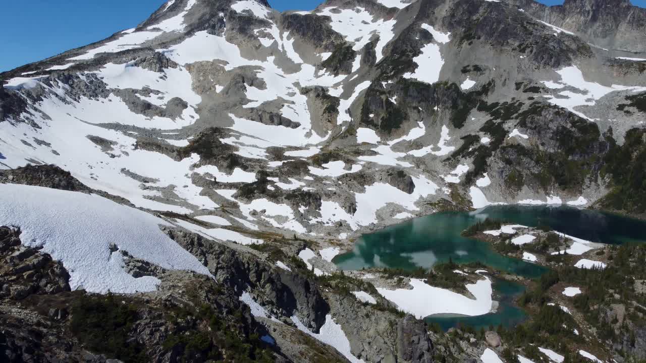 브리티시 컬럼비아 캐나다 4k의 눈부신 푸른 호수와 함께 눈 덮인 슈거로프 산 정상의 샷을 패닝하는 공중 드론