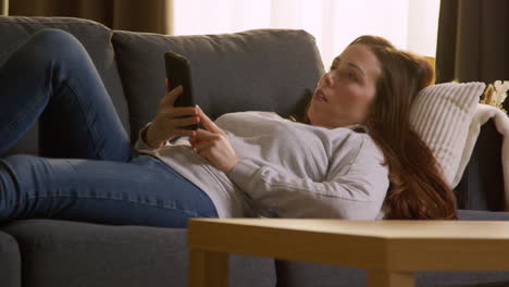 Woman Lying On Sofa At Home Fed Up And Bored With Time Wasted Using Mobile Phone To Check Social Media Message And Scroll Online 1