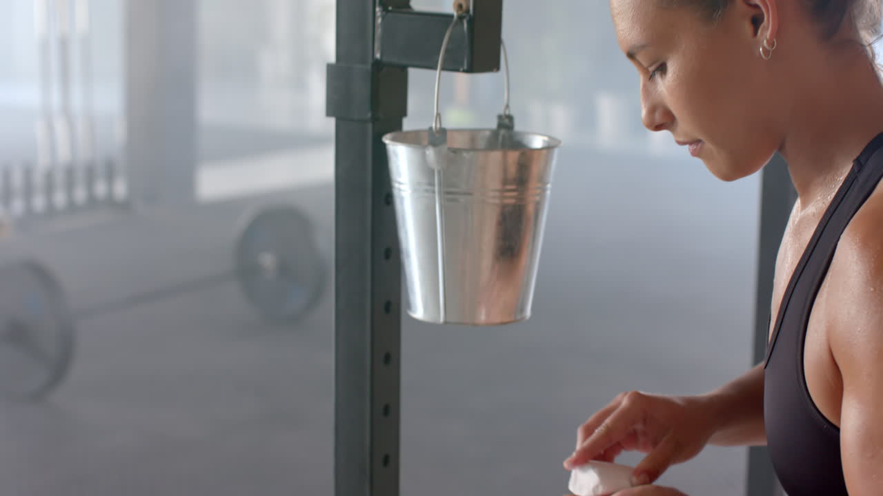 At gym, strong fit woman focusing on workout near metal bucket and barbell