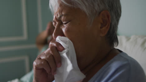 Senior-mixed-race-woman-coughing-in-bed-husband-ill-in-background