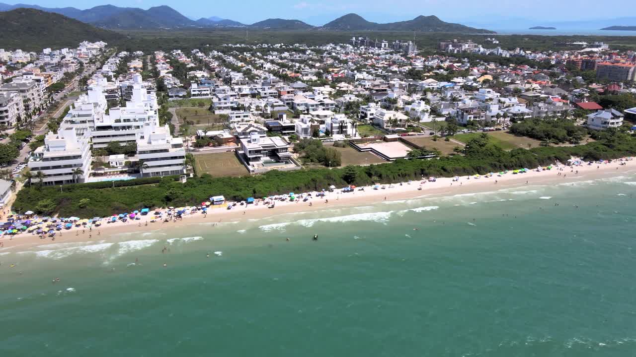 escena de altitud de drones aéreos de playa turística con muchos alojamientos frente al mar, edificios de vuelo y casas con gente divirtiéndose en la playa en florinópolis jurere internacional