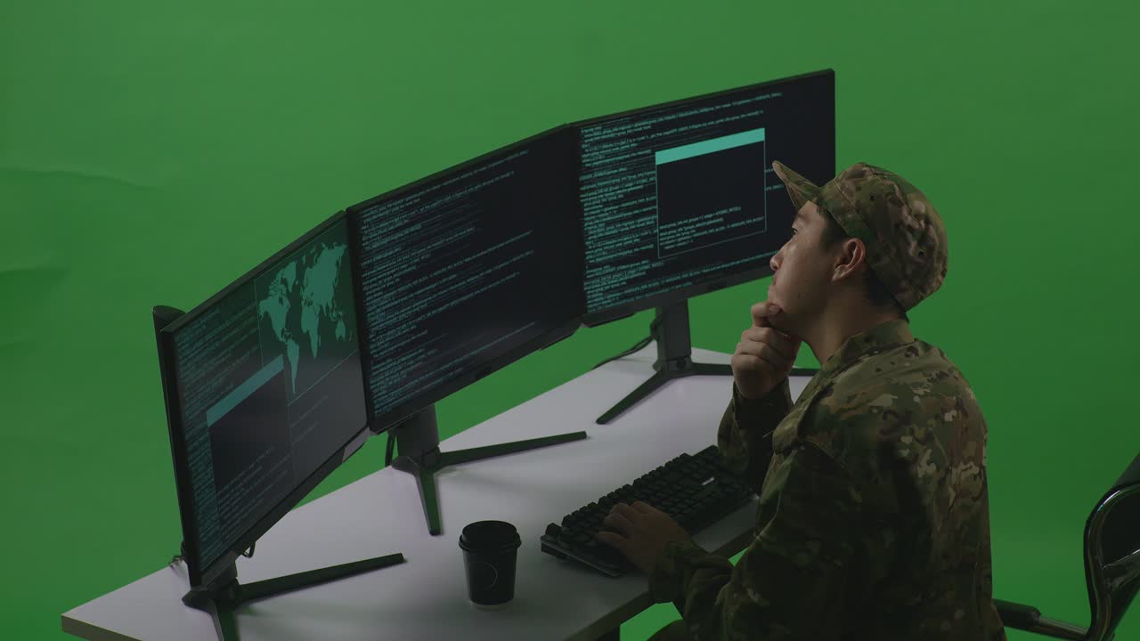 Side View Of Asian Man Soldier Developer Thinking About Something While Write Code With Multiple Computer Screens In Green Screen Studio