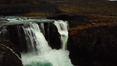 aerial drone view over water flowing down a large waterfall, in iceland