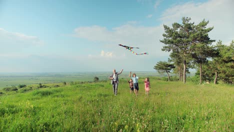 camera zooming on caucasian senior man and his grandchildren running in the park while they are flying a kite on a sunny day