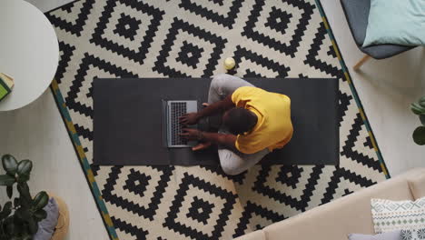 Black-Man-Using-Laptop-and-Drinking-Water-on-Floor-at-Home