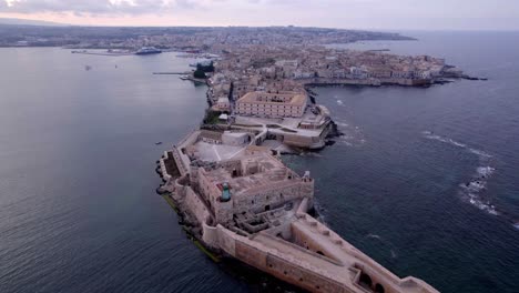 Antena-Hacia-La-Ciudad-Histórica-De-La-Isla-De-Ortigia-Al-Atardecer,-Sicilia-Italia