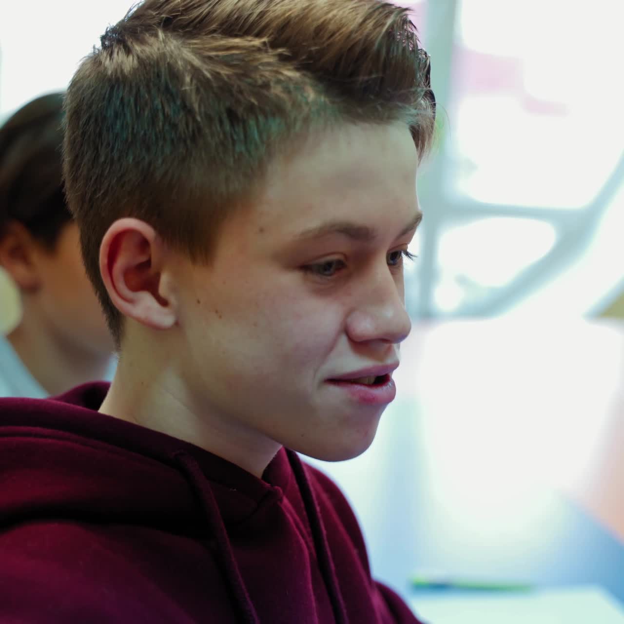 Teenage boy in the classroom. Student sitting at the table and talking to the teacher at school. Creative thinking of a pupil. Education concept.
