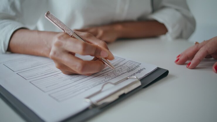 Primo piano di mani che scrivono documenti di richiesta sulla scrivania. Paziente che firma il modulo assicurativo.