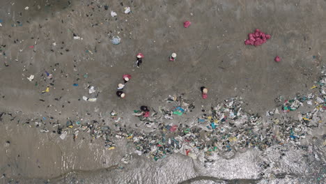 aerial top down of southeast asian villagers in bamboo hats cleaning plastic trash from beach