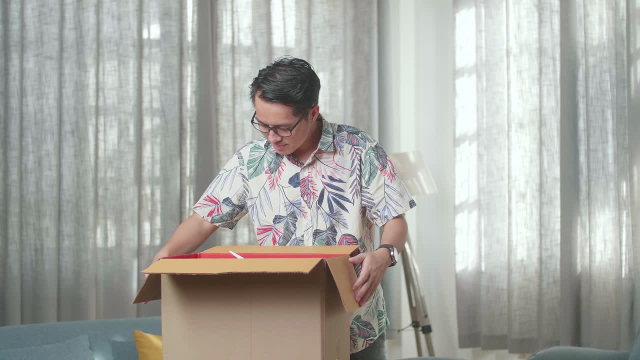 hombre asiático mudándose a una casa nueva desempaquetando la caja de cartón y sacando cosas de ella