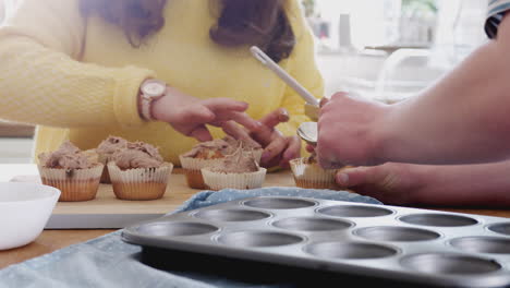 close up of young downs syndrome couple decorating homemade cupcakes with icing in kitchen at home