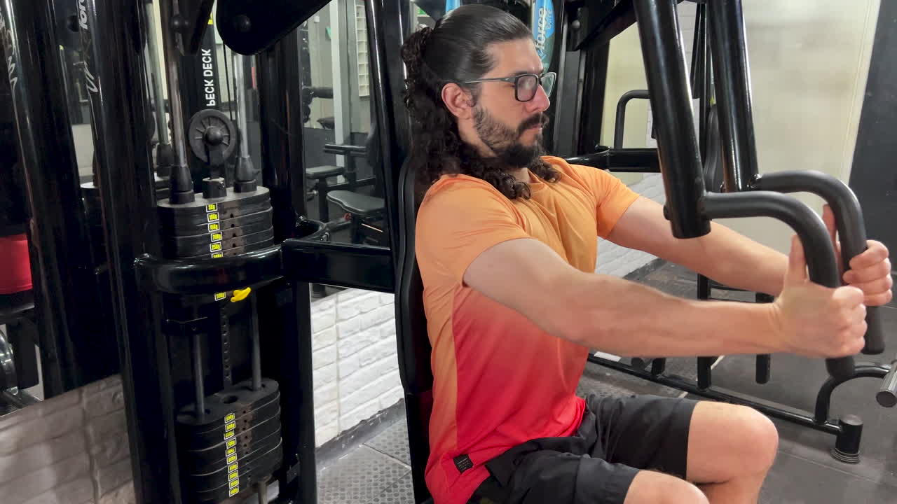 hombre latino con barba y cabello largo realizando ejercicio de crucifixión en la máquina - peck deck fly
