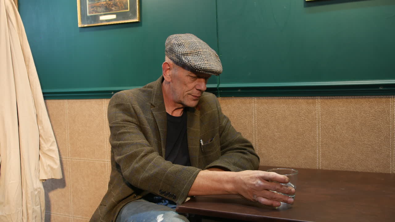 An elderly man sits alone in a pub, drinking from a glass