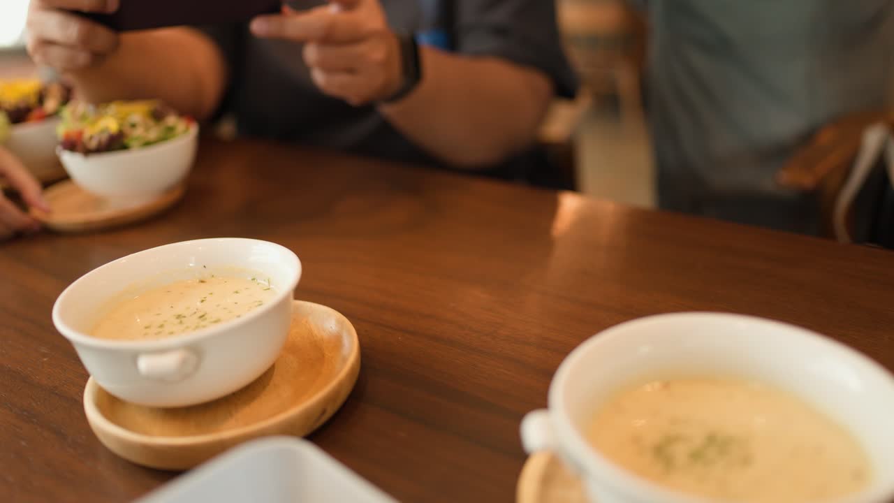 Hand places creamy soup bowl on wooden plate at sunlit cafe table, warm inviting atmosphere