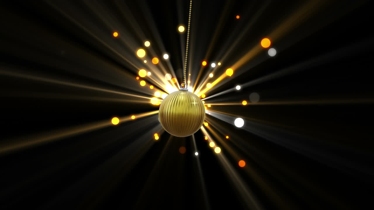 Swinging gold christmas bauble over starburst and light spots on black background