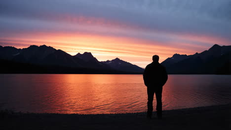 man silhouetted against a vibrant sunset over a lake and mountains