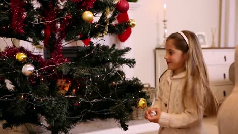 little girl hanging decorations on christmas tree