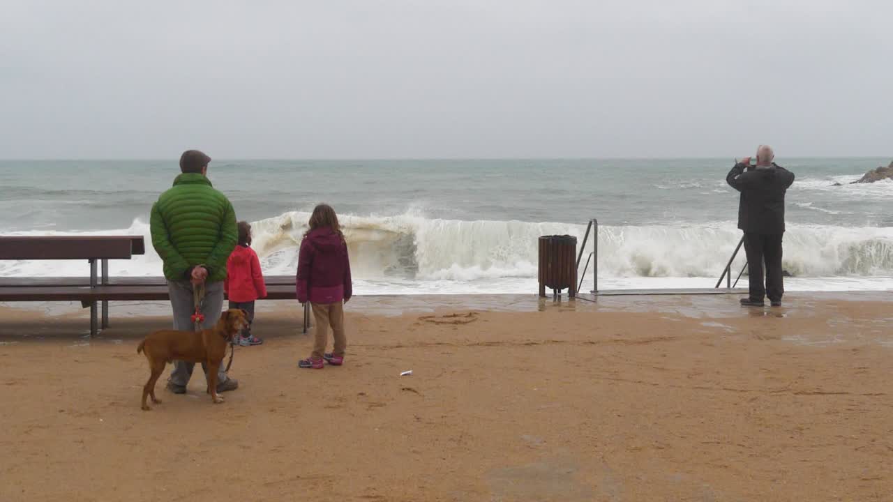 gente de atrás viendo la tormenta y las olas rompiendo en la playa