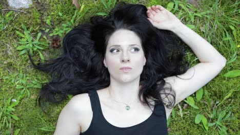 beautiful free spirited female laying on the grass in nature, looking at the trees, close-up on the face