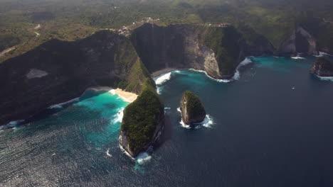 drone flying up tilt down above kelingking beach on nusa penida island over the seashore green peninsula yellow sand