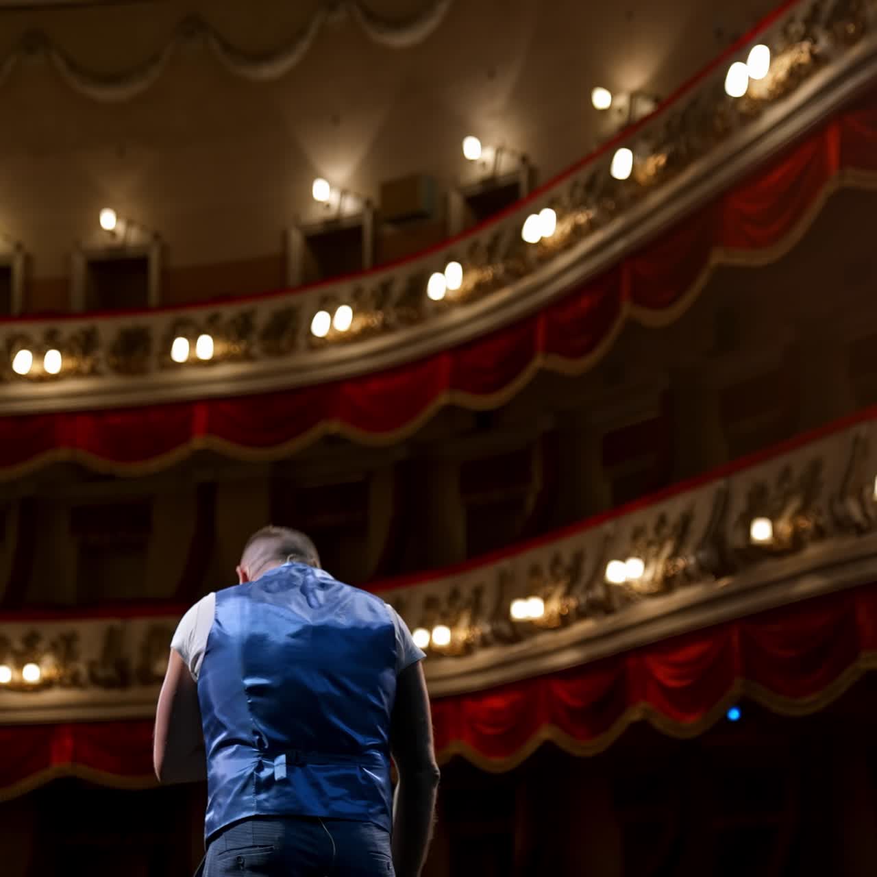 Man rehearses on stage. Actor performing from the scene gesticulating a lot on modern theater background. Rear view
