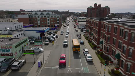 Forwards-tracking-of-yellow-school-bus-in-streets-of-urban-neighbourhood.-Buildings-with-red-brick-facades.-Boston,-USA