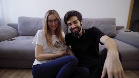 hermosa pareja joven con su gato en su sofá de la sala de estar hablando con la cámara