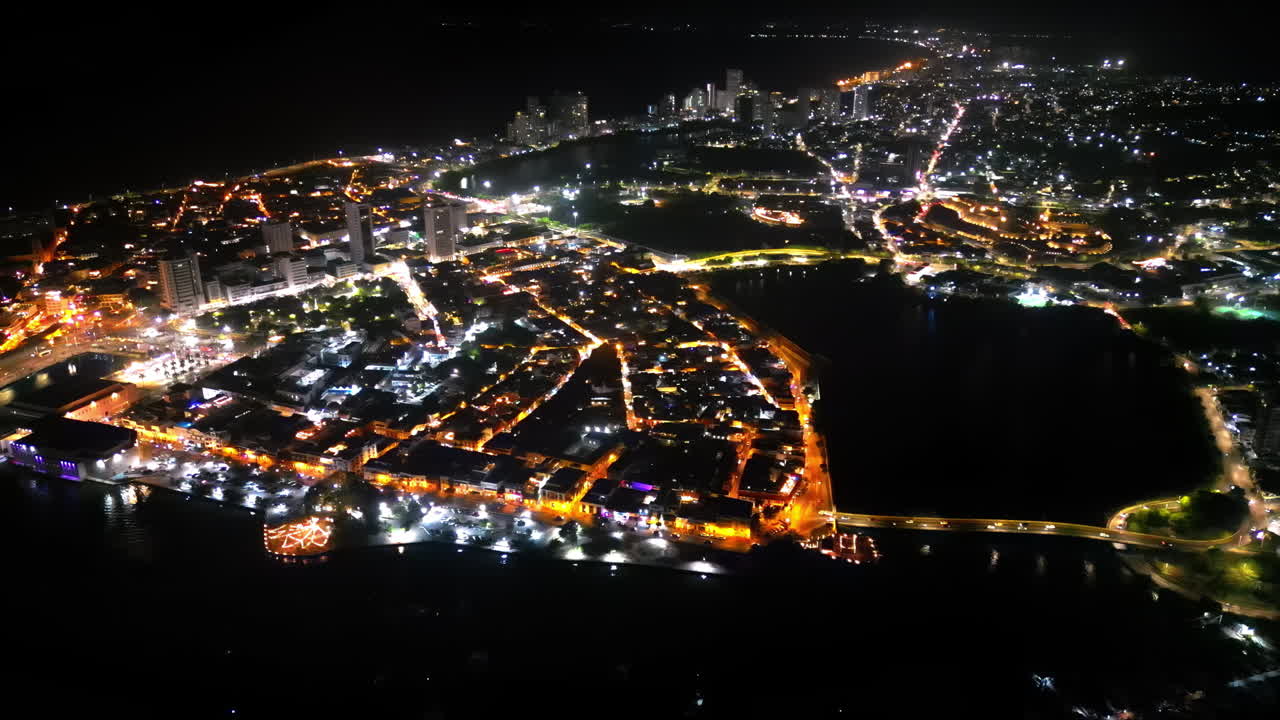 Aerial drone view of Cartagena at night showing both the colonial old town and the modern skyline glowing with orange and white lights