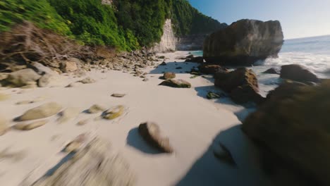 FPV-drone-horizontal-shot-flying-over-sandy-beach-with-waves-crashing-along-Suwehan-beach,-Nusa-Penida,-Bali-on-a-sunny-day