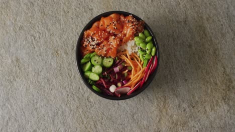 Composition-of-bowl-of-rice,-salmon-and-vegetables-with-chopsticks-on-white-background