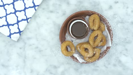 a person hand picking up a churro and dripping it into melted chocolate, close up