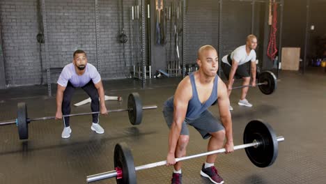 diverse male group lifting barbells, free weight training at gym, in slow motion