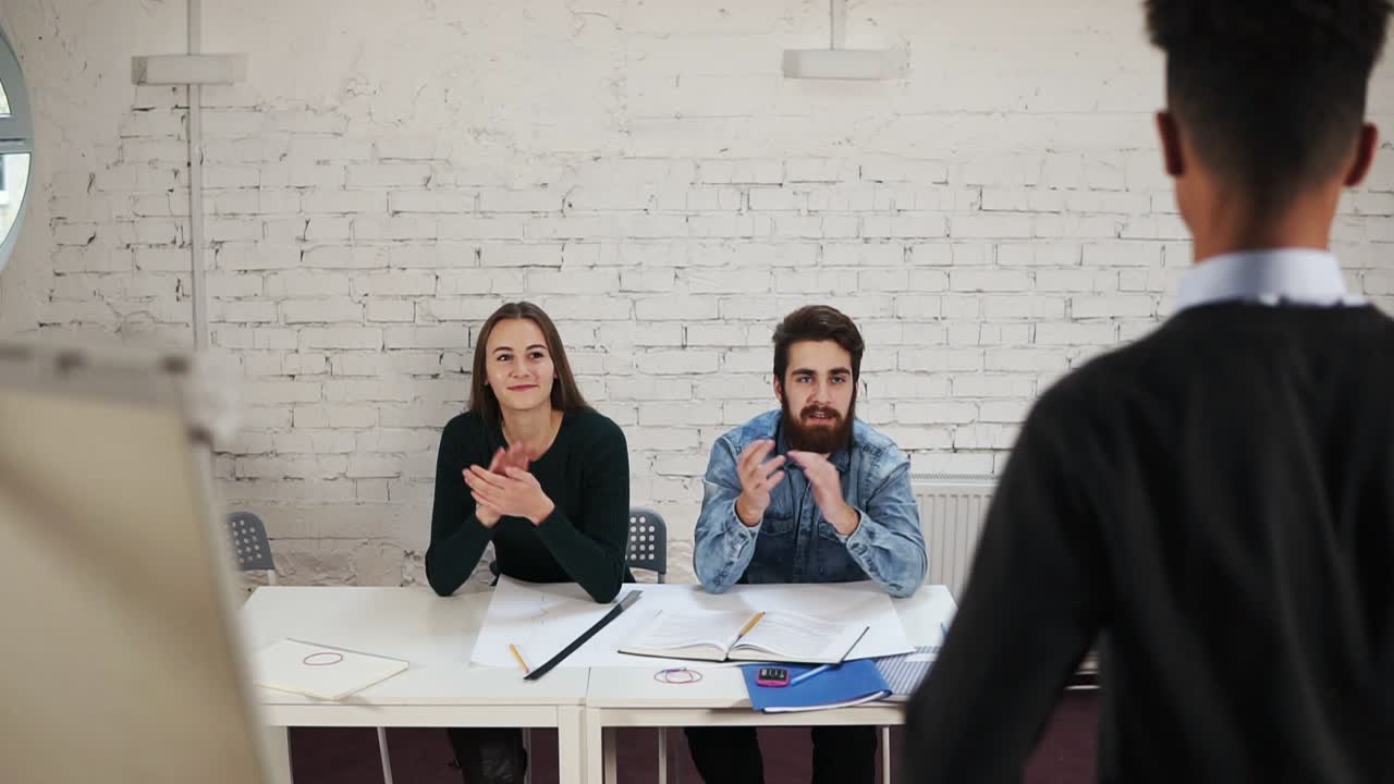 vista trasera del sofá de piel oscura de pie junto al flipchart recibiendo aplausos de sus clientes. trabajador de oficina afroamericano