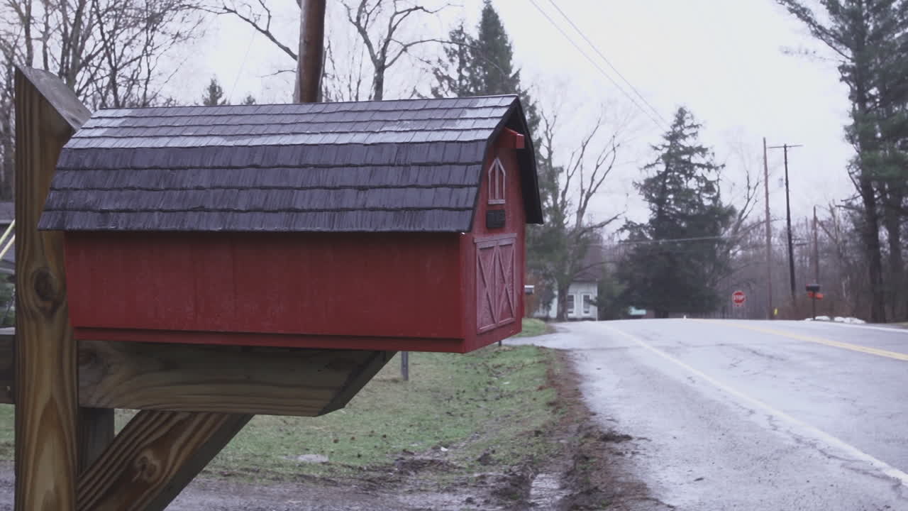 Pan from right to left over barn road revealing close up of red mail box shaped like a miniature barn