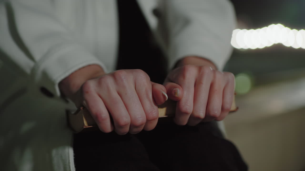 Close up woman in white coat firmly gripping book, distant bokeh lights softly glowing, highlighting serene night mood, capturing subtle hand details and calm warm atmosphere