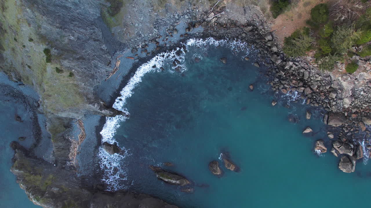 Aerial view of a rocky coastline bay with turquoise water and crashing waves