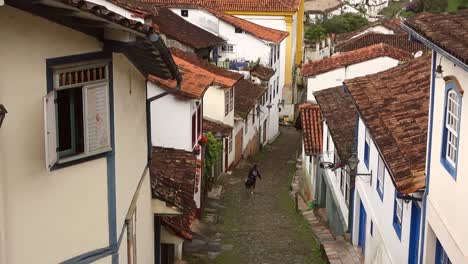 traveler-walks-down-narrow-cobbled-slope-between-historic-buildings-in-Ouro-Preto,-MG,-Brazil