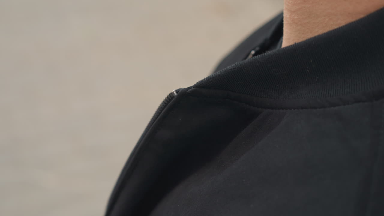 남자가 옷깃을 정리하는 모습, 재킷 깃을 정리하는 남자의 클로즈업, 검은색 스웨터를 입은 남자가 부드럽게 목 부분을 매만지는 동작, 남자가 부드러운 손짓으로 재킷 깃을 정리하는 클로즈업 장면