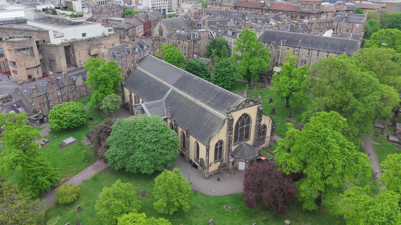 Cinematic drone orbit of Greyfriars Kirkyard, Edinburgh’s historic cemetery. Atmospheric aerial view of gothic tombstones, old church, and surrounding stone walls