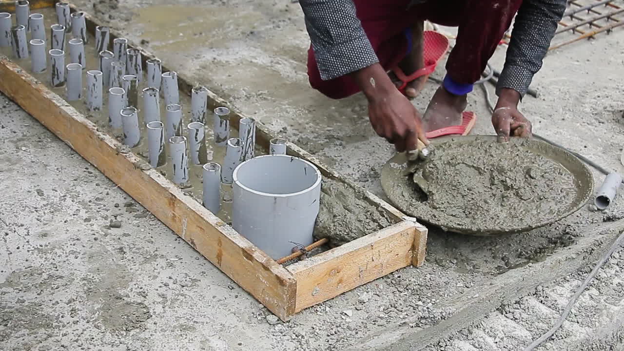Indian mason worker placing concrete around pipes in a slab with hands-on leveling technique