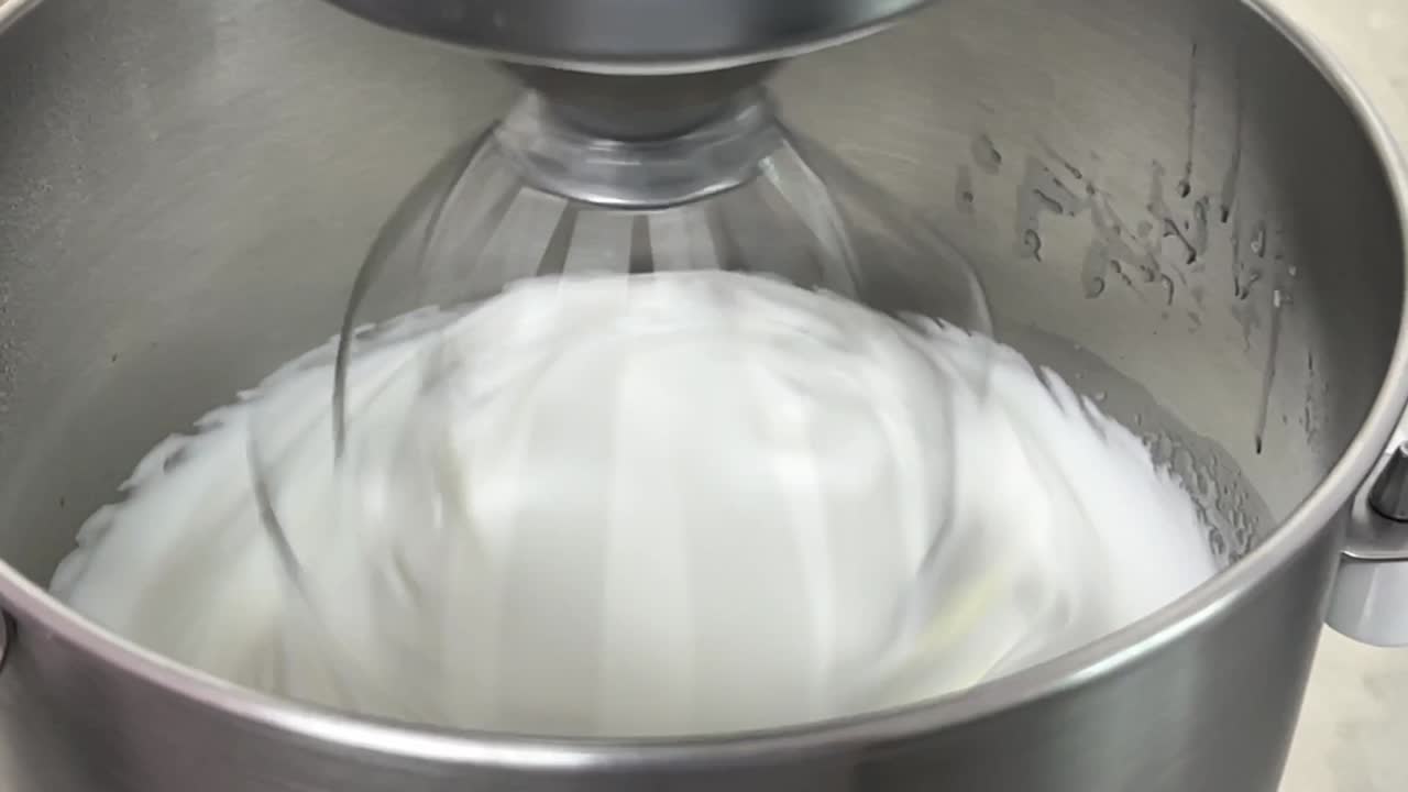 Commercial kitchen close up shot of electric mixer mixing egg white and sugar until it is glossy peak and stiff peak, preparing meringue buttercream