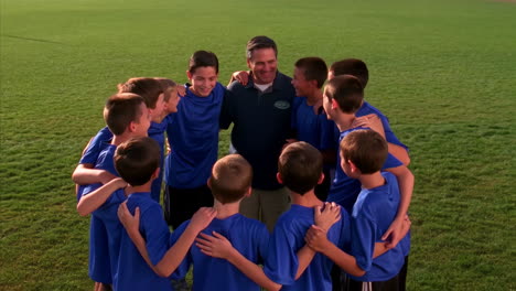 youth soccer team huddles with their coach on a field