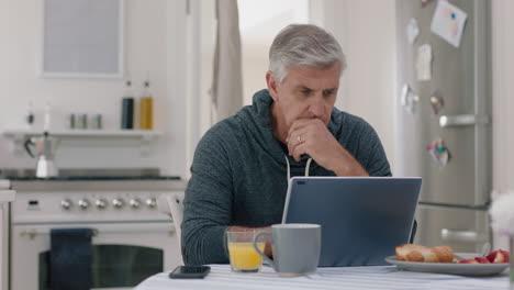 happy-mature-man-using-laptop-computer-at-home-typing-messages-browsing-online-enjoying-working-in-morning-at-breakfast-4k-footage