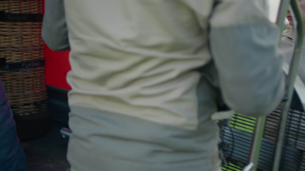 Close up of workers removing hot air balloon engine from trailer surrounded by green field, focusing on gloved hands, orange tarp flap, and metallic engine part during setup process