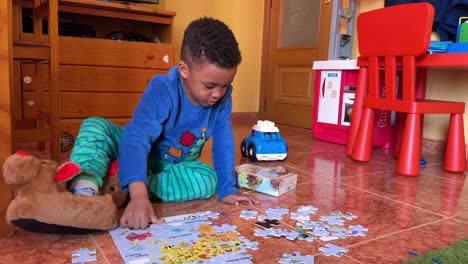 a cute 4-year-old toddler sitting on the floor at home doing a puzle. he is wearing winter clothes and curly hair. 4k