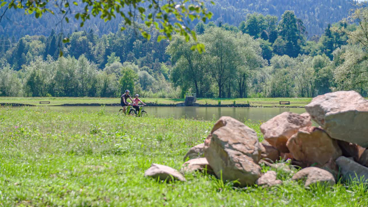 couple cycle by the lake. Relax and enjoy the peaceful nature. Panning shot