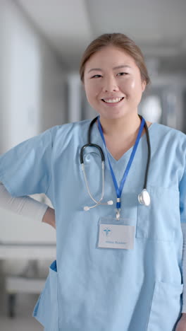 vertical video of portrait of happy asian female doctor in hospital corridor, slow motion