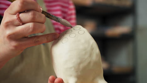 female hand decorating clay mug using paintbrush. pottery design. closeup shot
